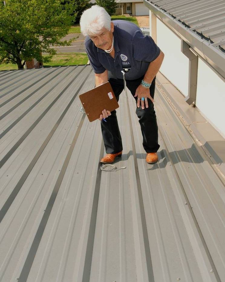 An inspector examines a metal roof for hail damage