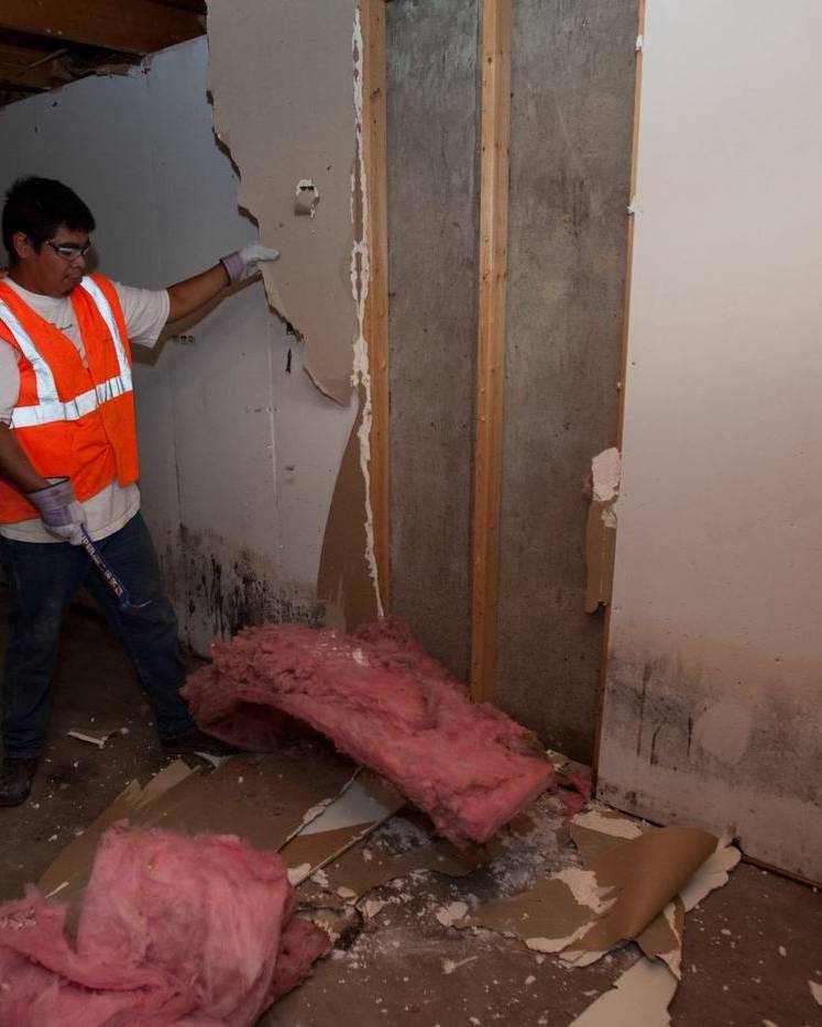A worker tears out water-damaged drywall